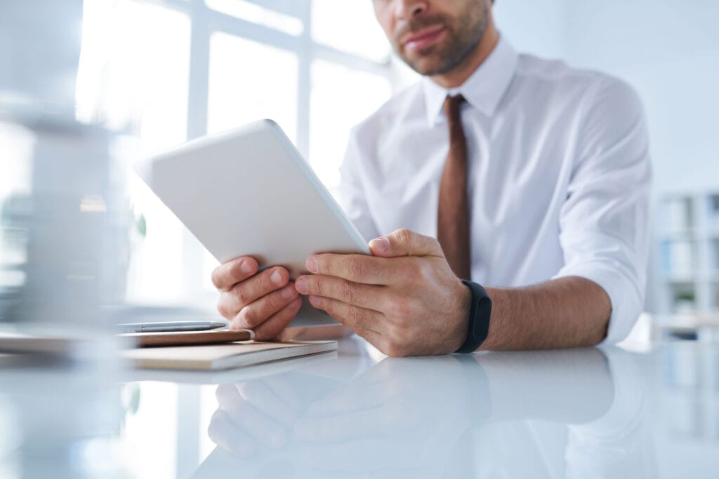 A imagem mostra um empreendedor em seu escritório, mexendo no tablet. Ele está pesquisando sobre pix garantido.