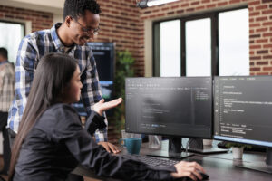 A imagem mostra um homem em pé e uma mulher sentada. Eles estão em um escritório, em frente ao computador, analisando os dados do sistema api da empresa.