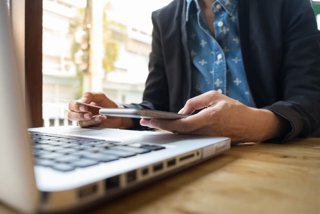 Na imagem, temos o sindico de um prédio em seu escritório, na frente do seu computador, com um tablet em uma das mãos e um cartão em outra. Ele está usando a melhor conta digital para condomínios.