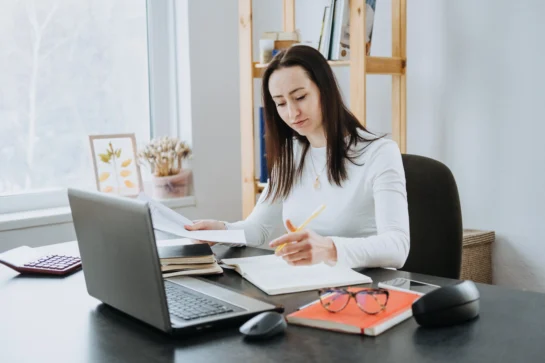 Mulher realizando a gestão financeira de conta digital para ONG. Ela está em mesa, preenchendo papéis.