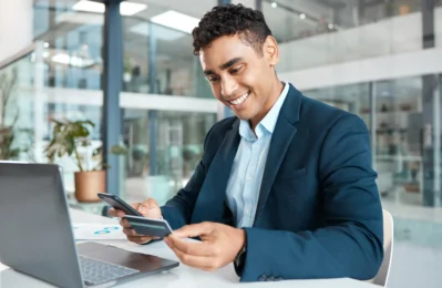 Empreendedor sorridente usa cartão e celular no escritório, representando praticidade e gestão financeira com conta para microempresa.