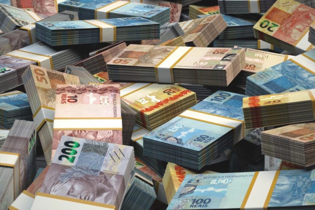 A imagem mostra vários malotes de dinheiro, notas de 200, 100, 10 e 20 reais, representando o real digital.