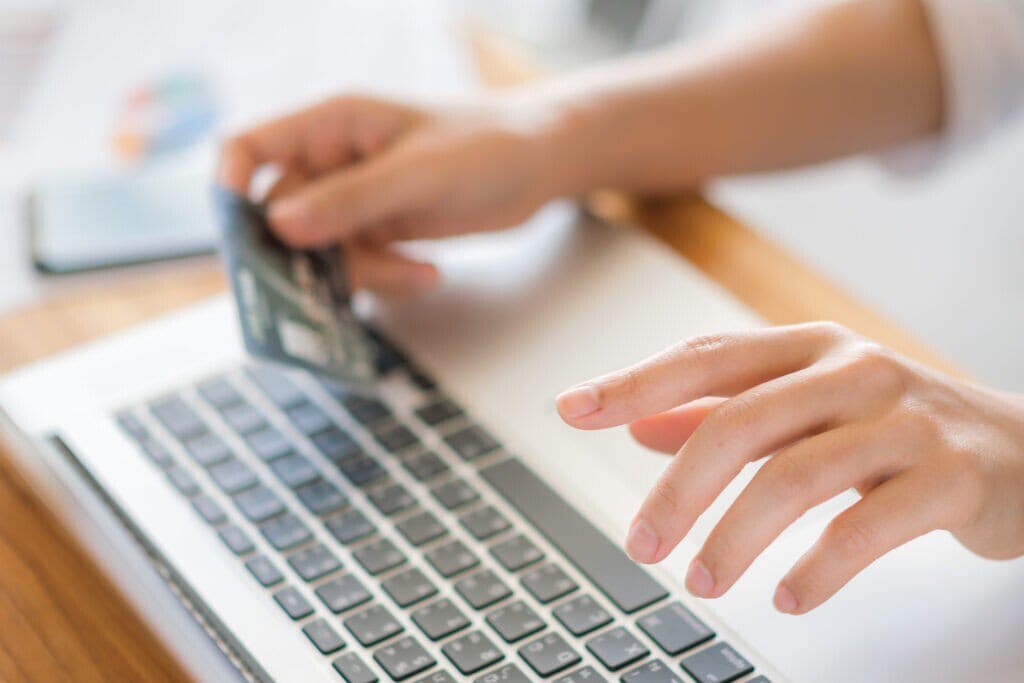 A imagem mostra um cliente com seu cartão de crédito, na frente do computador. Ele está finalizando uma compra, escolhendo formas de pagamento para loja virtual.