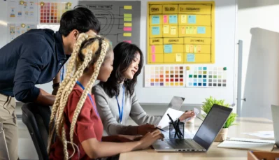 Três professores reunidos em frente a um notebook avaliando o sistema de gestão escolar.