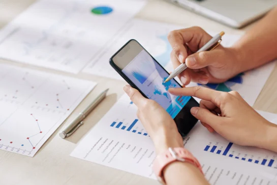 Duas pessoas avaliando dados econômicos em um celular, destacando a praticidade de um aplicativo de gestão financeira.