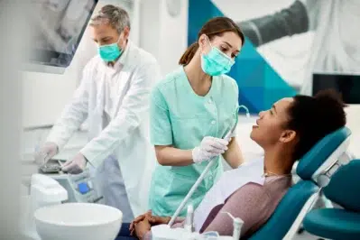 Dentista realizando consulta em paciente, enquanto profissional ao lado realiza gestão financeira para dentistas.