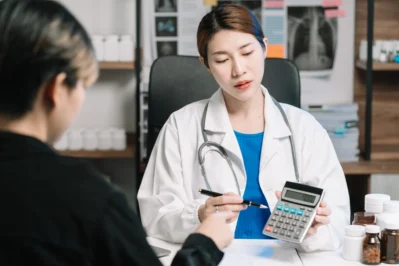 Cena de médica utilizando calculadora para auxiliar na gestão financeira para médicos em um consultório com o paciente.