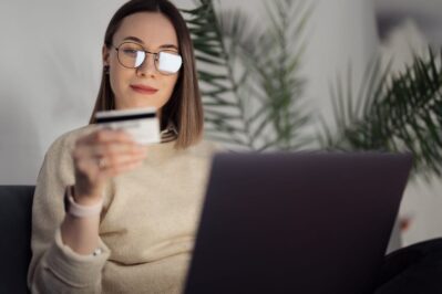 Uma mulher segura seu cartão de crédito enquanto faz uma compra online, aproveitando as promoções do cyber monday.