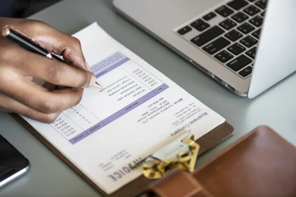 Empresario preenchendo nota fiscal com caneta, com papel na prancheta.