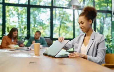 Mulher sorrindo em escritório, abrindo um notebook, simbolizando negócios, reuniões e o processo de abrir CNPJ.