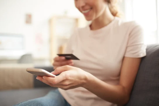 Mulher segura cartão e celular sorrindo, descobrindo o que é link de pagamento e suas vantagens.