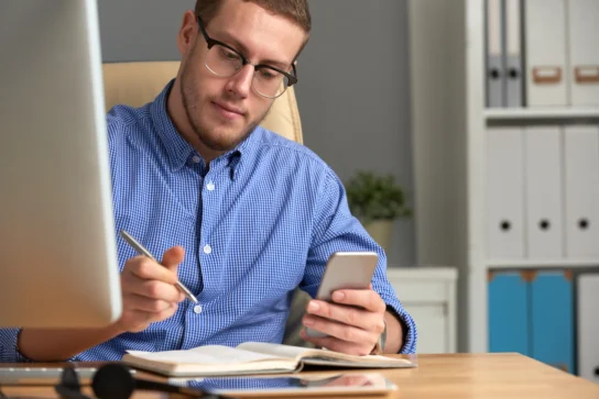 Homem está com celular na mão checando o seu lembrete de cobrança.