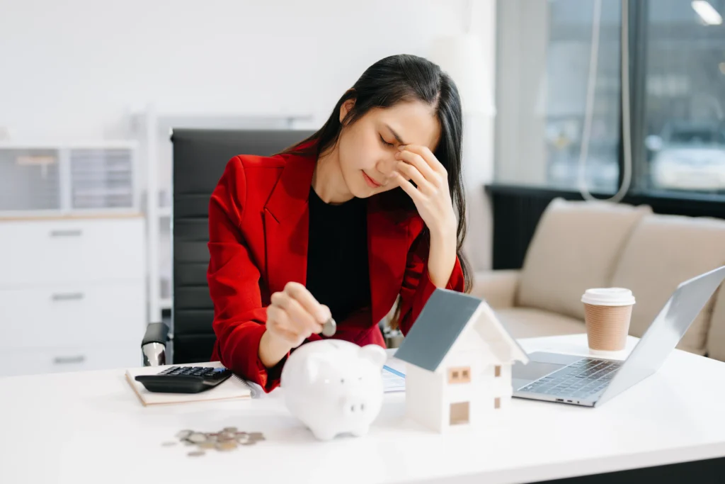 Mulher refletindo sobre finanças enquanto coloca moedas em um cofrinho, simbolizando qual a diferença entre poupança e investimento.