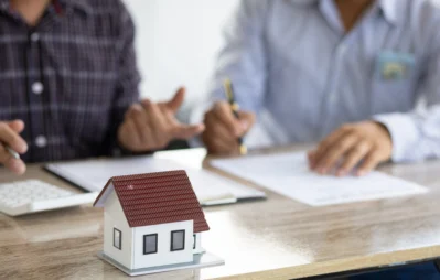 Homens entendendo como cobrar juros de aluguel atrasado, sentados em uma mesa, com uma mini casa em cima de uma mesa.