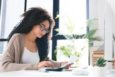 Empresária negra com óculos analisando recibos e usando calculadora, exemplificando como fazer um carnê de pagamento.