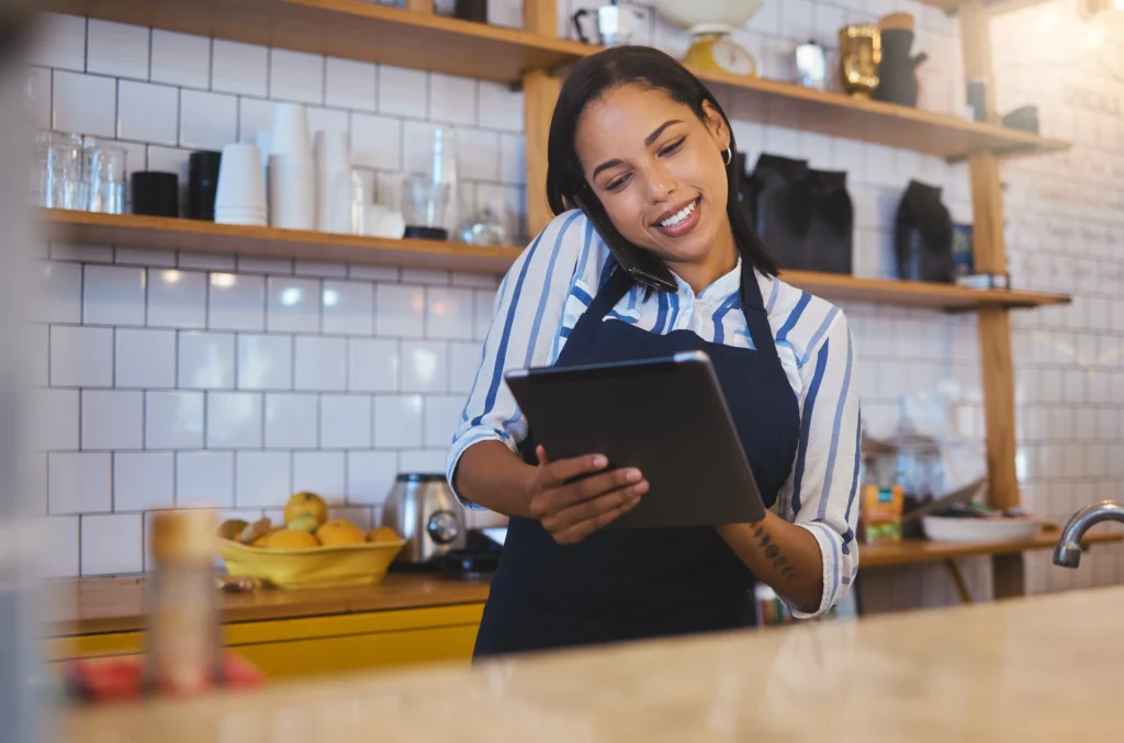 Funcionária usando celular e tablet para gestão do negócio, demonstrando como administrar financeiramente um restaurante.