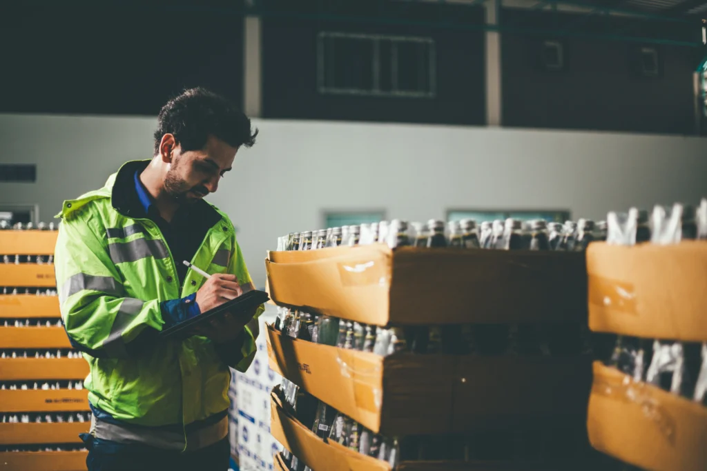 Trabalhador em frente a lotes de bebidas, fazendo controle de qualidade e utilizando ERP para distribuidora de bebidas.