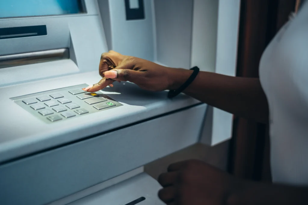 Mulher utilizando caixa eletrônico, digitando no teclado. Ela está digitando o código dos bancos para tirar dinheiro.