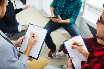 Grupo de pessoas, com as duas da frente escrevendo em uma prancheta. Estão escolhendo a melhor conta digital para associação.