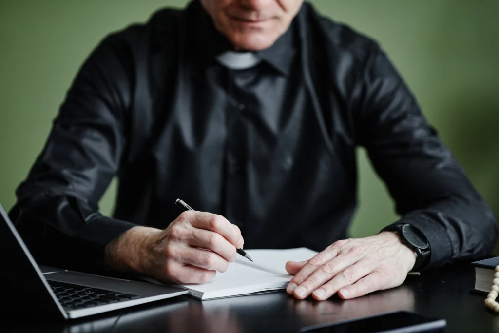 Padre usando caderno e laptop, ilustrando organização financeira com conta digital para igrejas. Fundo verde suave.