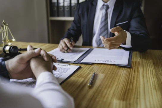 Profissionais sentados conversando. Assinam papéis em cima de mesa, conversando sobre contrato de contabilidade para advogados.