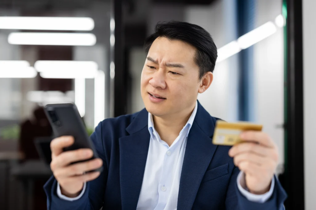 Homem analisando celular e segurando cartão, representando processo de contestação de pagamento online.