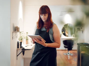 Mulher em um salão de beleza usando tablet, representando a gestão financeira para salão de beleza com tecnologia.