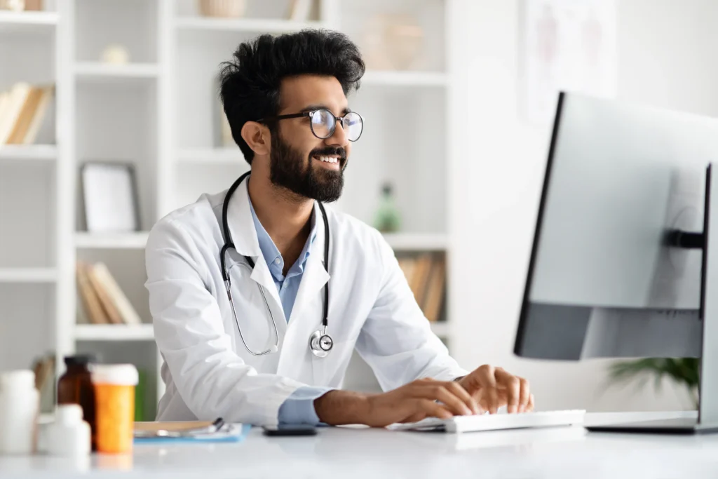 Médico digitando no computador em consultório, ilustrando uso da DMED, documento utilizado para prestar contas à Receita Federal.