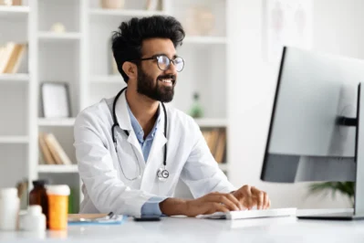 Médico digitando no computador em consultório, ilustrando uso da DMED, documento utilizado para prestar contas à Receita Federal.