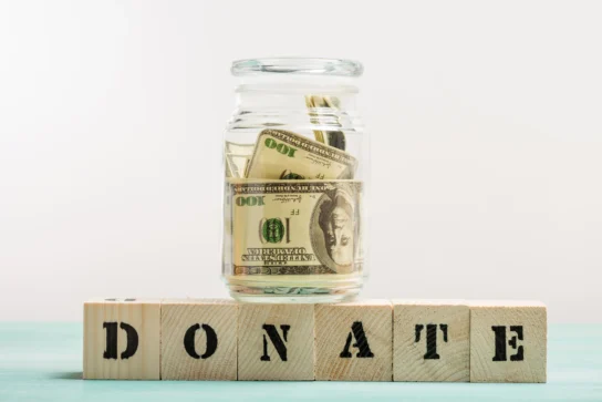 Pote com dólares e blocos escrito "Donate", representando como declarar doação recebida na declaração de imposto de renda.