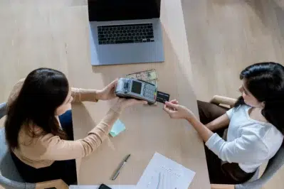 Melher segura a máquina e a outra passa cartão, representando o que é adquirente.