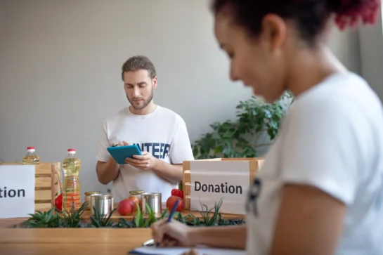 Voluntários organizam alimentos e produtos em caixas de doação em uma ONG, em um ambiente que levanta dúvidas se ONG paga imposto.