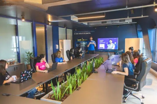 Reunião de equipe no Asaas com apresentação sobre a missão, visão e valores do Asaas em ambiente moderno e colaborativo.