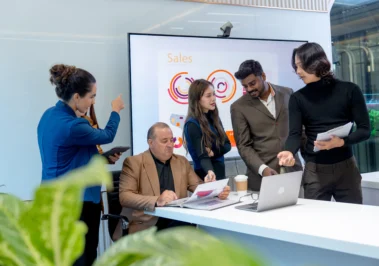 Profissionais discutem gráficos de vendas em reunião sobre fusão e aquisição de empresas em ambiente corporativo moderno.