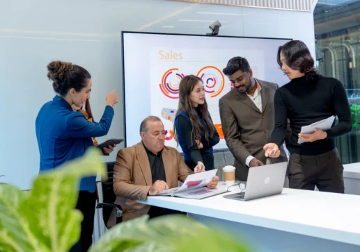 Profissionais discutem gráficos de vendas em reunião sobre fusão e aquisição de empresas em ambiente corporativo moderno.