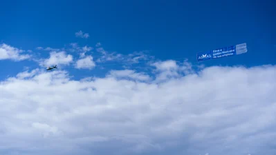 Avião sobrevoando o céu com banner publicitário do Asaas in Rio promovendo gestão financeira para empresas.