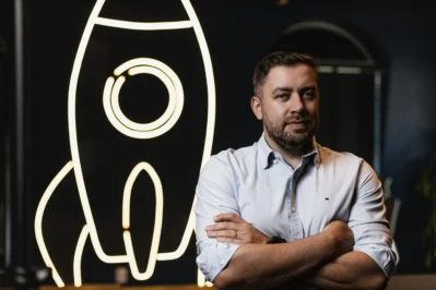 Júnior Beltrão, CRO do Asaas, em frente a um painel iluminado em formato de foguete, simbolizando crescimento e inovação da fintech.