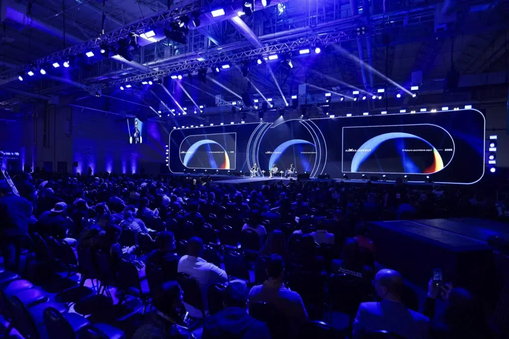 Público acompanha painel do Asaas Connect 2025 em auditório iluminado, com palestrantes no palco e telões ao fundo.