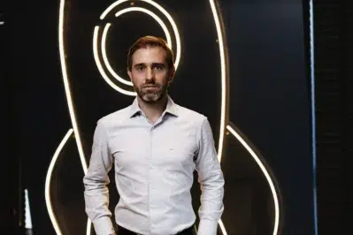 Foto de João Vitor Possamai, em frente a um fundo de led que desenha um foguete. Ele olha para foto e veste terno.