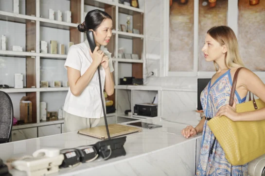 Recepcionista ao telefone atendendo cliente no balcão, ilustrando o que é essencial para um bom atendimento ao cliente.