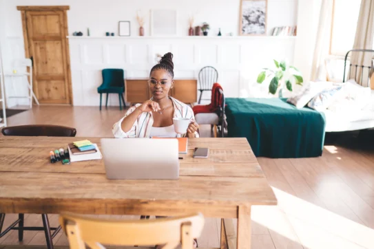 Pessoa em home office trabalhando no notebook com uma xícara na mão, pois possui trabalho remoto e híbrido.