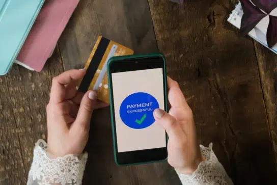 Pessoa usando aplicativo para passar cartão pelo celular enquanto segura um cartão para confirmar o pagamento.