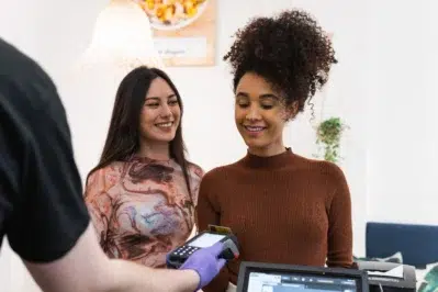 Duas mulheres realizando compra em maquininha, mostrando como funciona o pagamento parcelado no cartão de crédito.