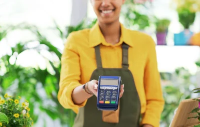 Vendedora sorridente segurando terminal de pagamento, ilustrando busca por maquininha de cartão com menor taxa de juros.