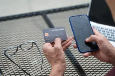 Pessoa usando cartão e smartphone para transformar celular em maquininha em uma mesa ao ar livre.