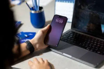 Mão segurando um celular em frente ao notebook, representando o tema volume de transações via Pix cresce 55% em 2025.