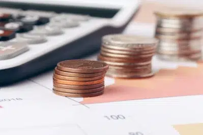 Moedas empilhadas e calculadora sobre gráfico financeiro, ilustrando planejamento para o imposto de renda 2026.