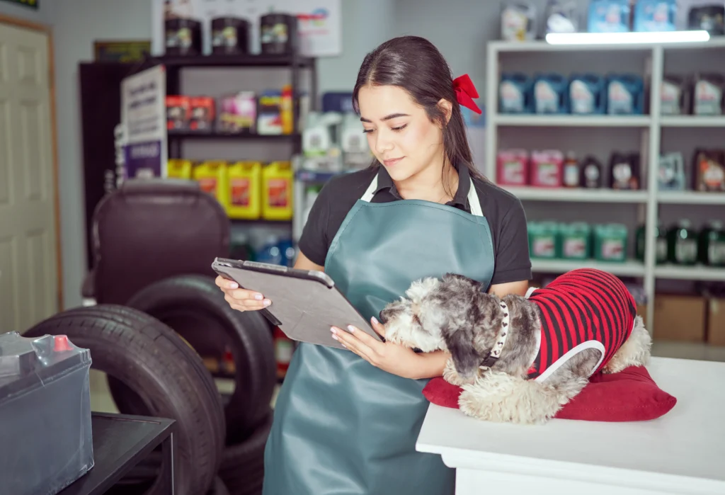 Profissional segurando o tablet ao lado de um cachorro. Está realizando a contabilidade para pet shop.