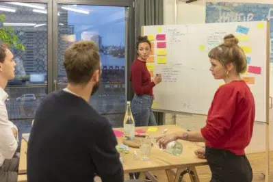 Equipe reunida em frente a um quadro preenchido com post-its, ilustrando na prática como fazer plano de ação 5w2h.