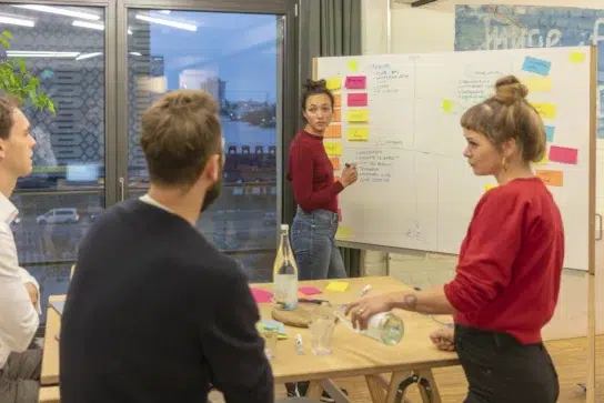 Equipe reunida em frente a um quadro preenchido com post-its, ilustrando na prática como fazer plano de ação 5w2h.